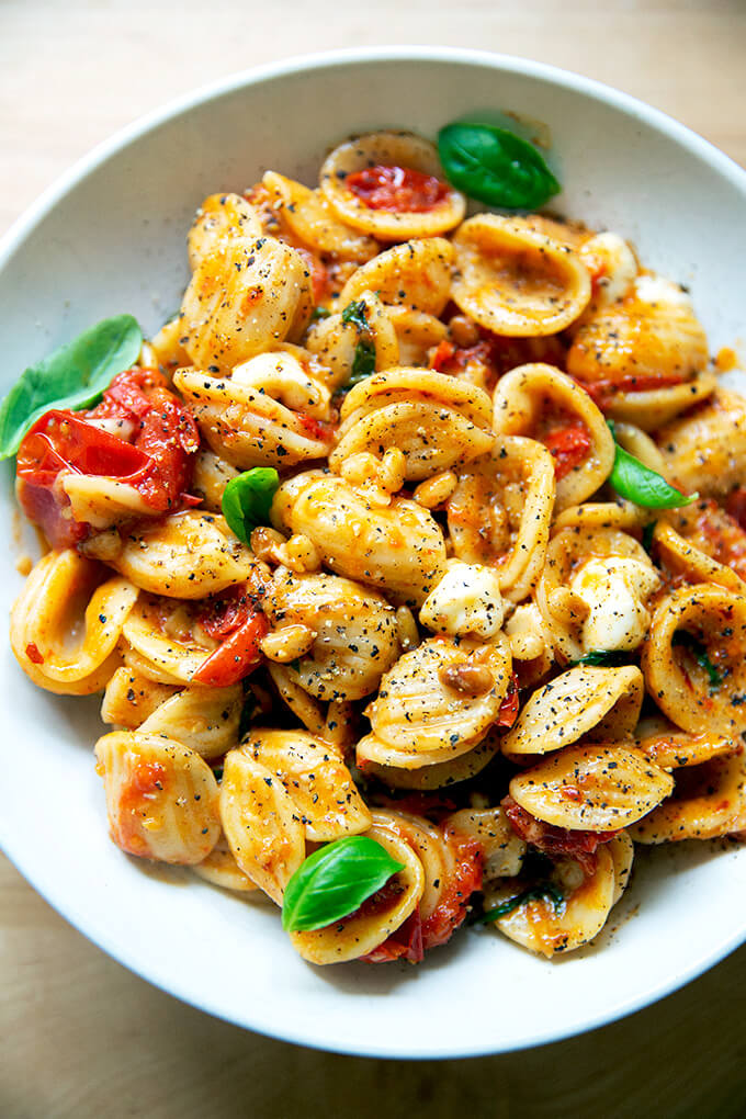 A bowl of pasta tossed with cherry tomato sauce, pine nuts, basil and mozzarella.