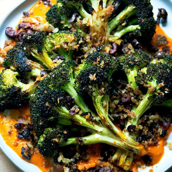 A plate of roasted broccoli steaks on tomato sauce topped with olive bread crumbs.