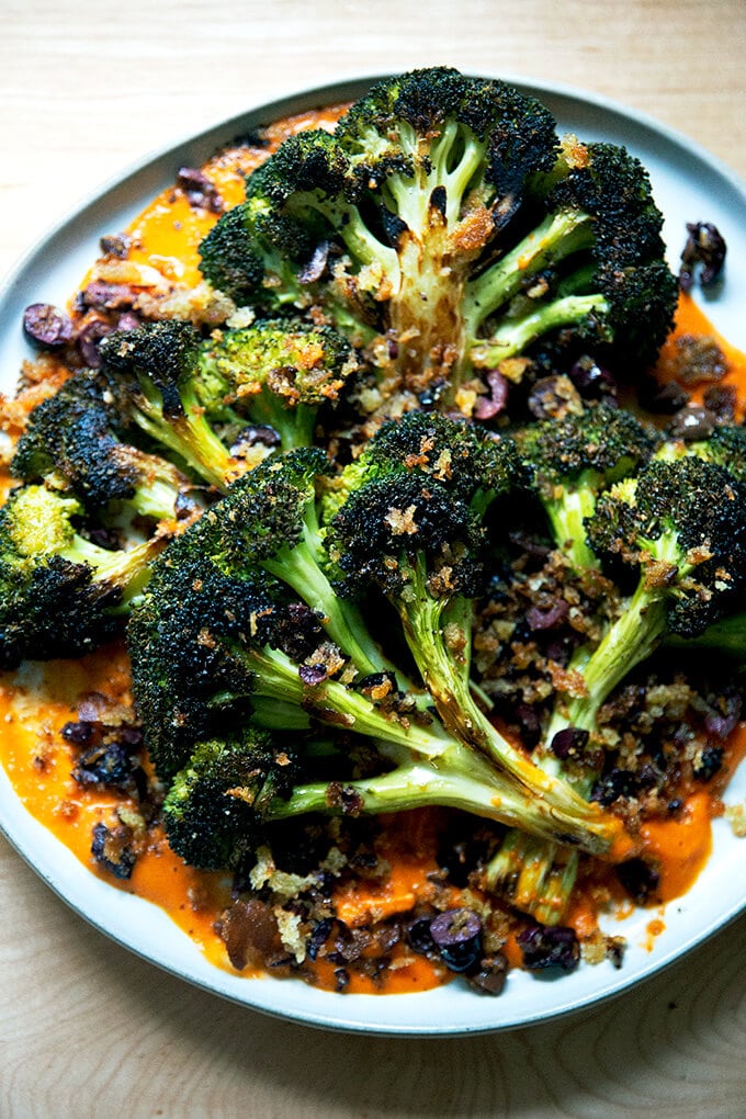 A plate of roasted broccoli steaks on tomato sauce topped with olive bread crumbs.