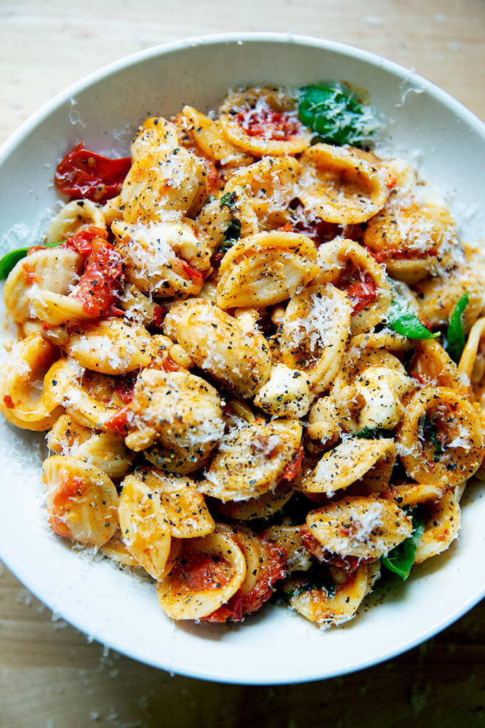 A bowl of pasta tossed with cherry tomato sauce, pine nuts, basil and mozzarella, topped with shaved parmesan.