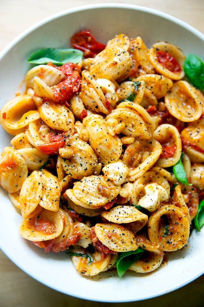 A bowl of pasta tossed with cherry tomato sauce, pine nuts, basil and mozzarella.