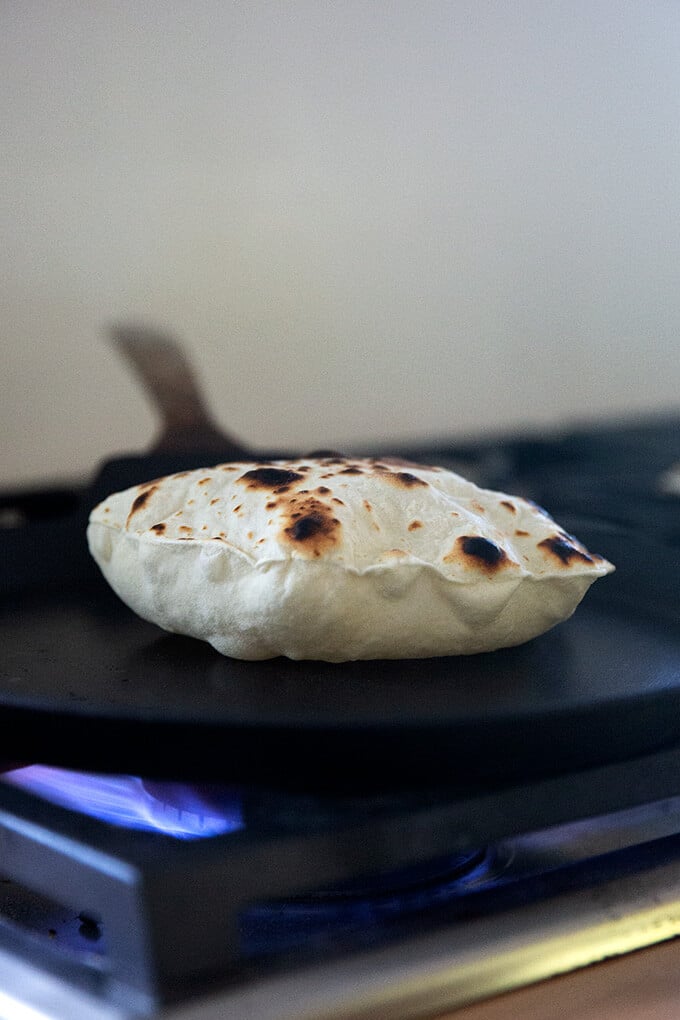 A sourdough flour tortilla cooking in a skillet stovetop.