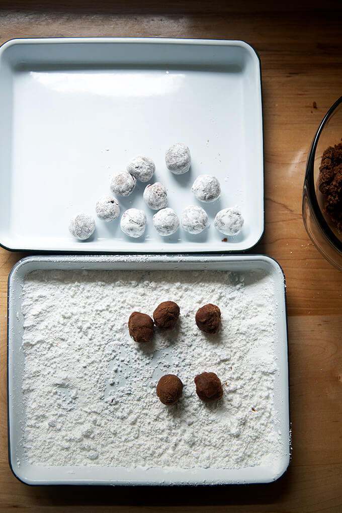 Two trays set up for the rum ball making process: one containing the finished rum balls; the other containing powdered sugar and the un-rolled rum balls.