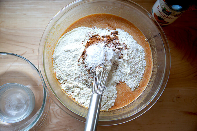 A bowl with a whisk and all of the ingredients for pumpkin bread inside.