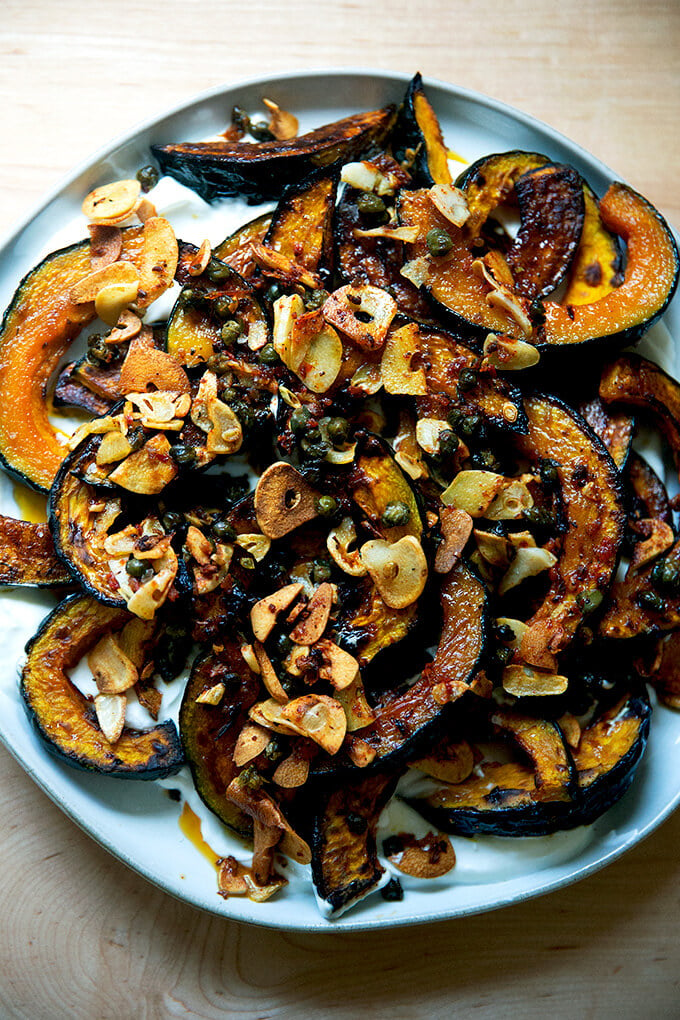 A plate of roasted Kabocha squash atop lemony yogurt sauce and sizzling garlic, capers, and Calabrian chili paste.