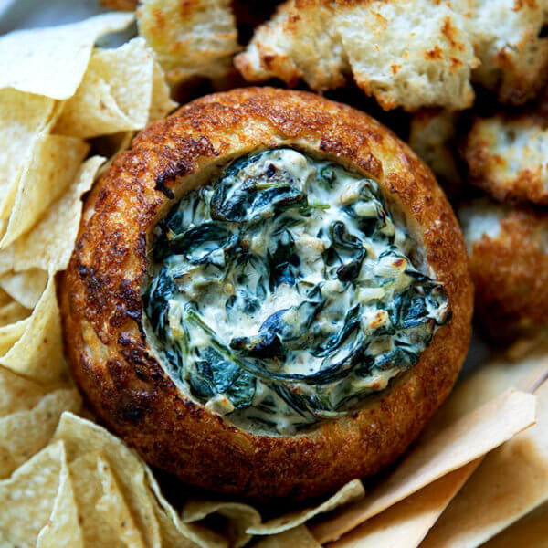 A bread bowl filled with spinach artichoke dip.