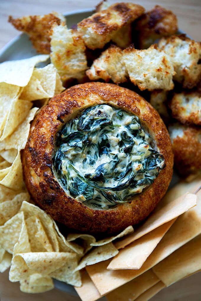 A bread bowl filled with spinach artichoke dip.