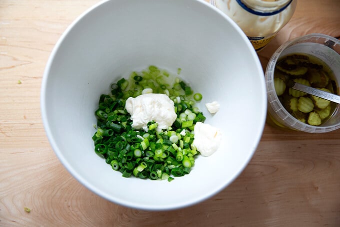 Scallions in a bowl with mayonnaise, pickle juice, and chopped celery.
