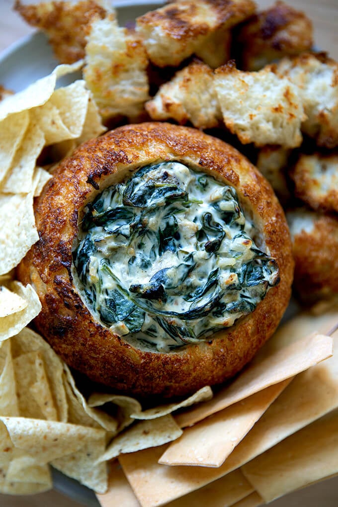 A bread bowl filled with spinach artichoke dip.