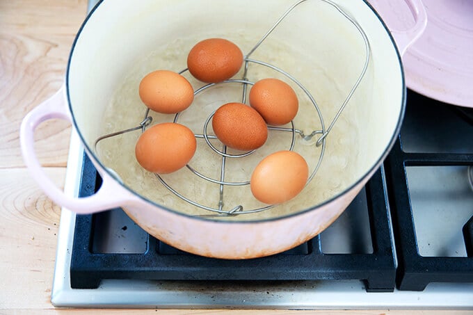 Eggs in a steamer basket in a pot on the stovetop.