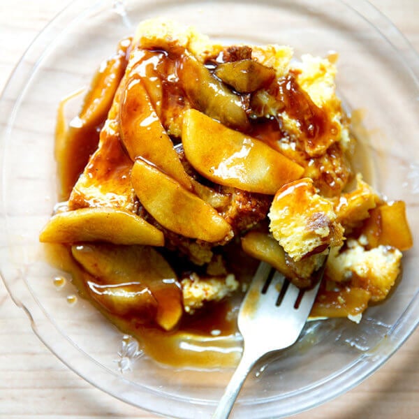 A plate of brioche bread pudding topped with apples sautéed in butter and caramel sauce.