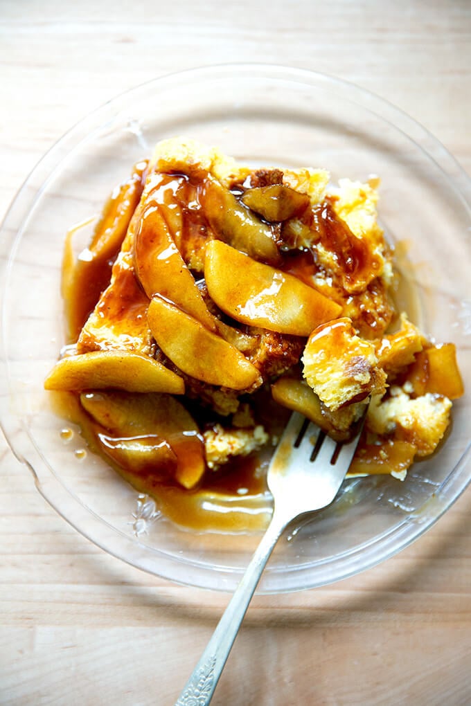 A plate of brioche bread pudding topped with apples sautéed in butter and caramel sauce.