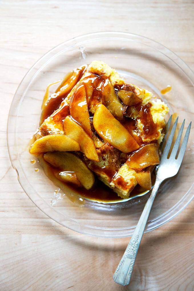 A plate of brioche bread pudding topped with apples sautéed in butter and caramel sauce.