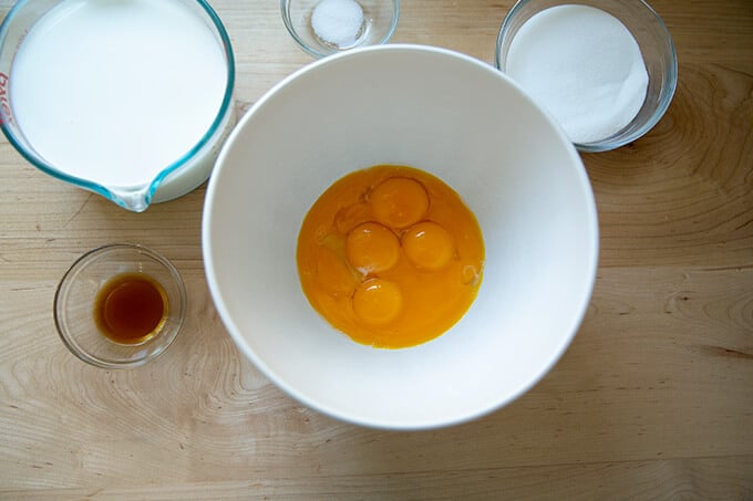 A bowl filled with egg yolks surrounded by the other ingredients for an egg custard.