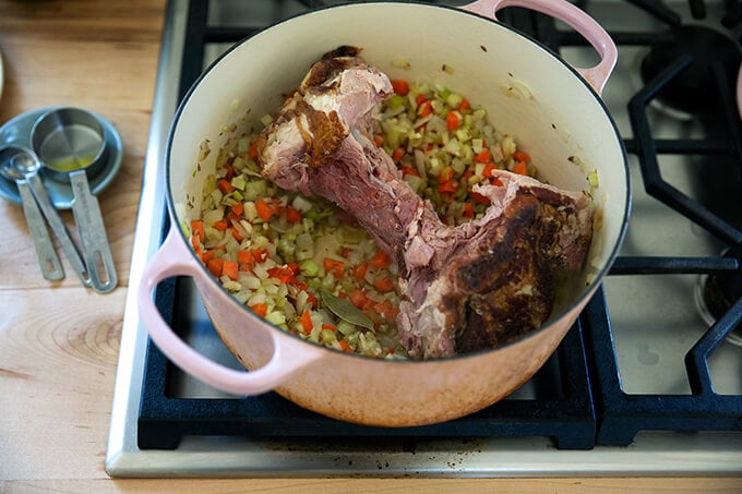 A large pot filled with sautéed vegetables and a ham bone.