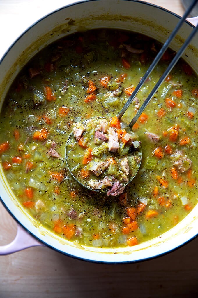 A large pot filled with split pea and ham soup with a ladle in it.