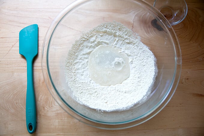 Adding water to flour and yeast in a glass bowl.