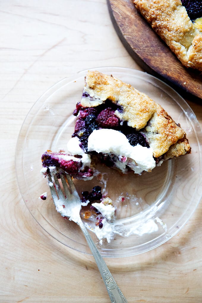 A half-eaten slice of mixed berry galette on a plate with a dollop of whipped cream on top.