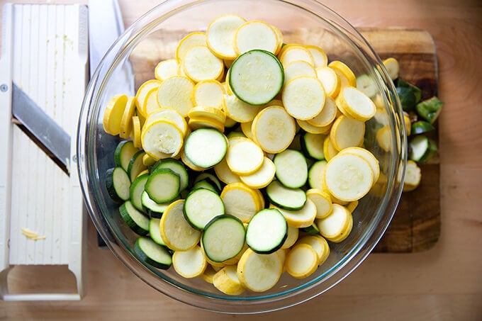 Sliced zucchini and summer squash in a large bowl aside a mandoline.