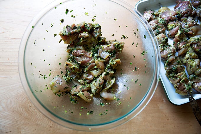 A bowl of chicken marinated with garlic and basil aside a tray of skewered chicken.
