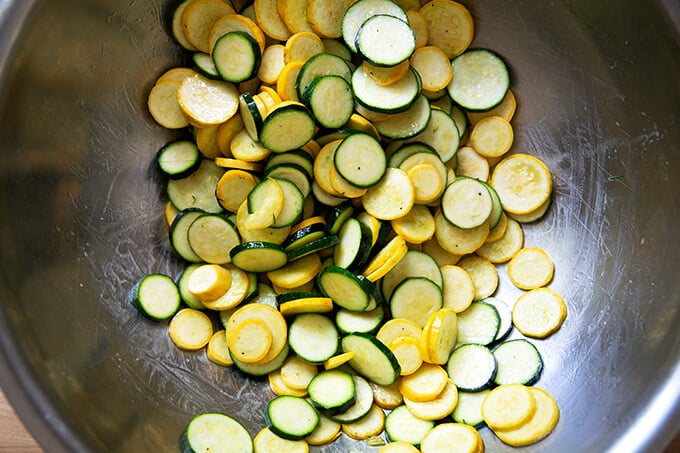 Sliced summer squash and zucchini in a large bowl dressed with olive oil and salt and pepper.