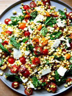 A platter topped with a raw corn salad made with tomatoes, feta, and lots of herbs.