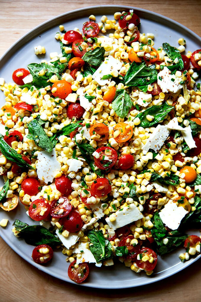 A platter topped with a raw corn salad made with tomatoes, feta, and lots of herbs.