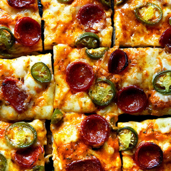 A sliced pepperoni and pickled jalapeño Detroit-style pizza on a board.