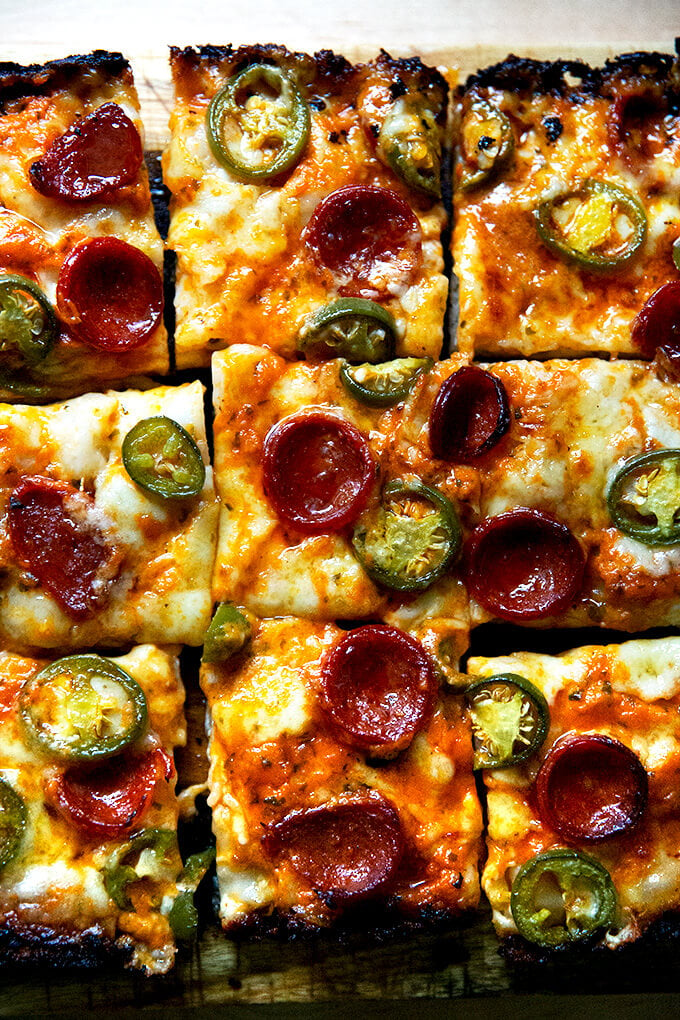 A sliced pepperoni and pickled jalapeño Detroit-style pizza on a board.