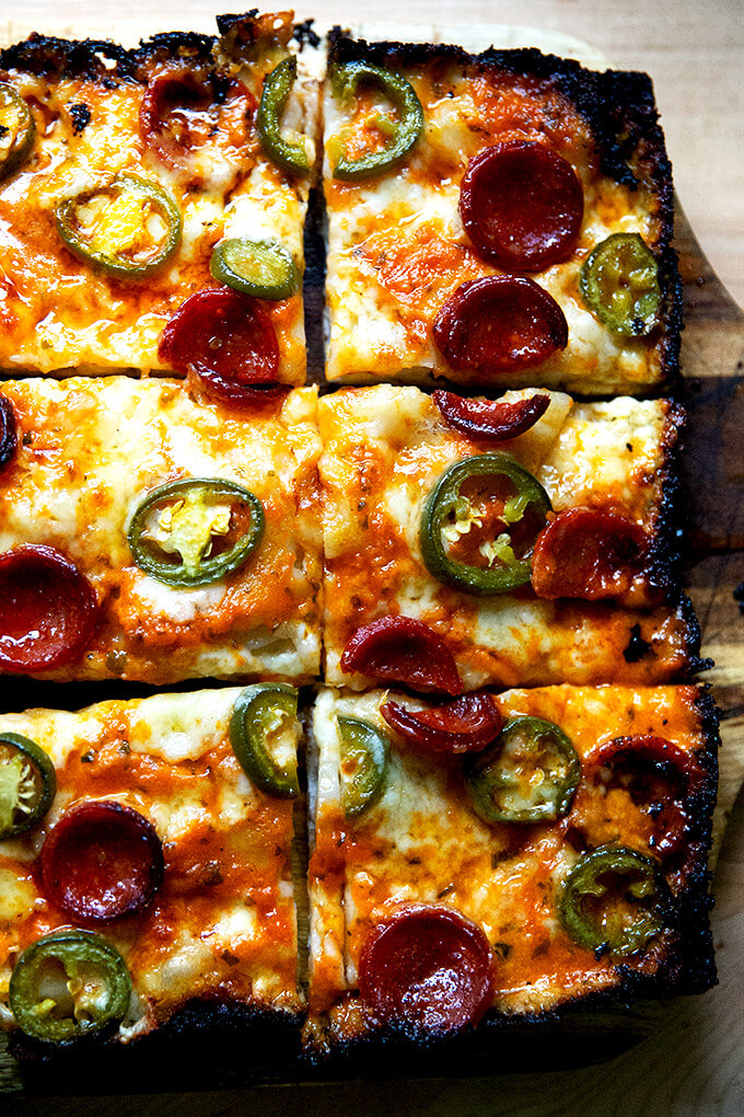 A sliced pepperoni and pickled jalapeño Detroit-style pizza on a board.