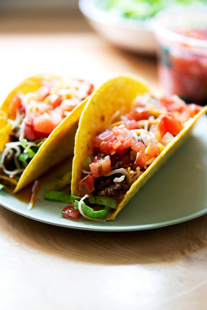 Two hard shell tacos filled with taco meat, cheese, and salsa on a plate.