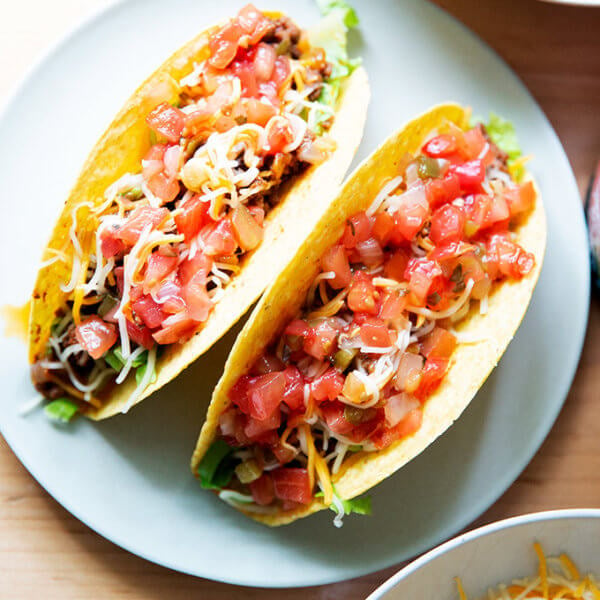 Two hard shell tacos filled with taco meat, cheese, and salsa on a plate.