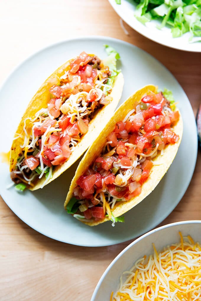 Two hard shell tacos filled with taco meat, cheese, and salsa on a plate.