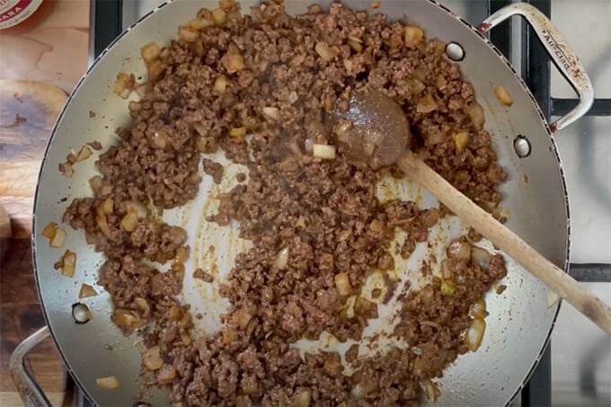 A sauté pan filled with onions, taco seasoning and ground beef.