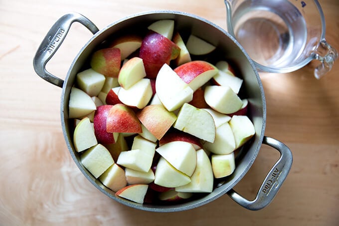 A pot holding chopped up apples aside a liquid measure holding a cup of water. 