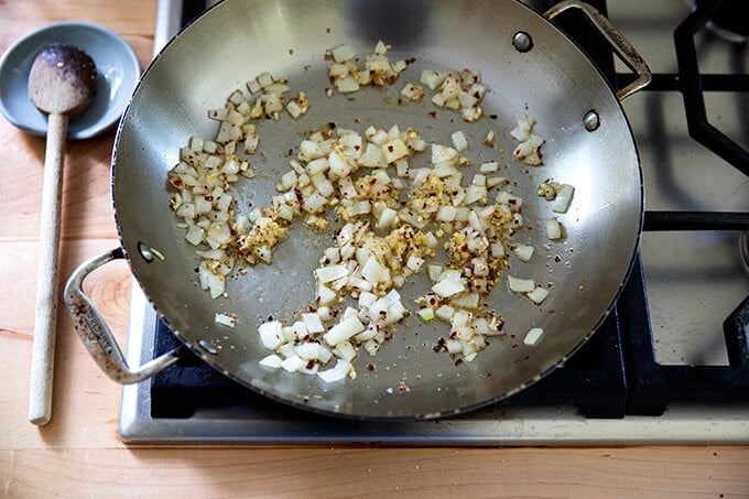 A skillet holding onions, garlic, ginger and crushed red pepper flakes.