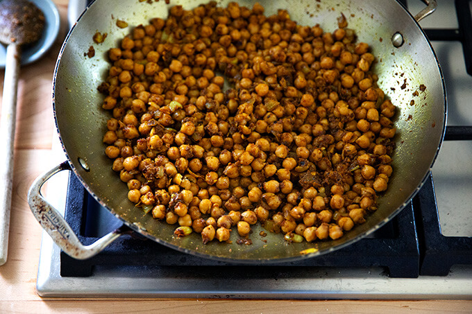 A skillet holding aromatics, curry spices, and chickpeas.