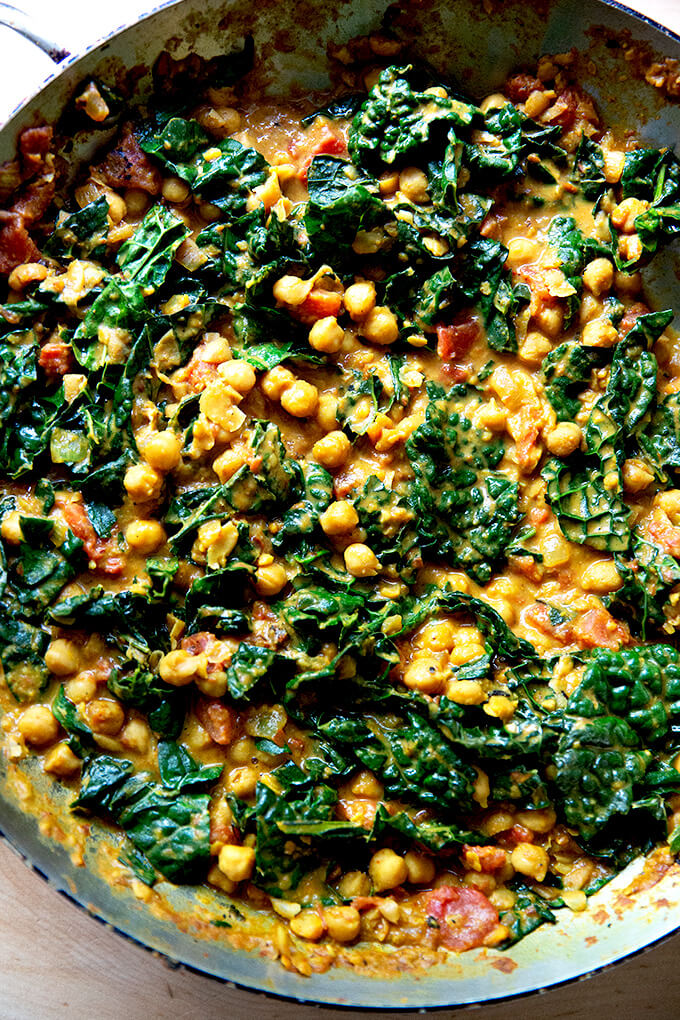 A skillet holding stewy, spicy chickpeas with kale and tomatoes.