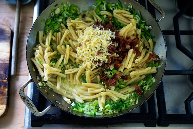 A skillet on the stovetop with leeks, lemon, bacon, and parmesan.
