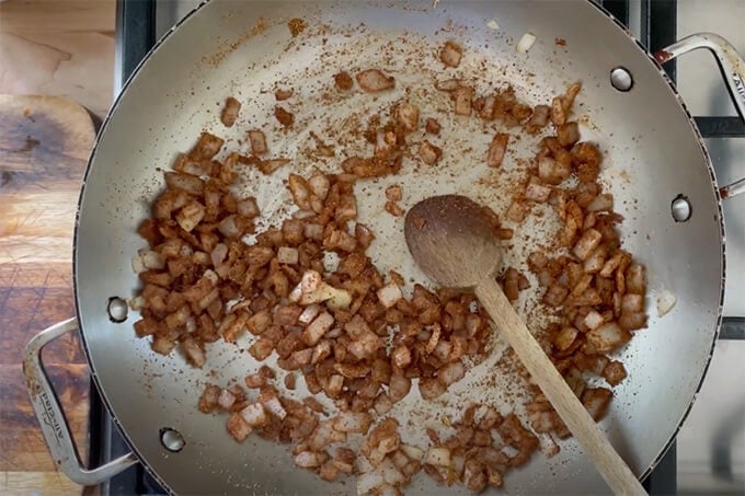 A sauté pan holding onions and taco spices. 