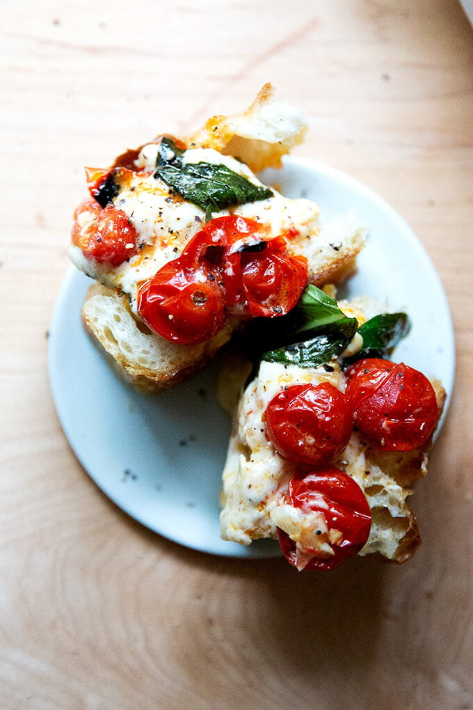 A plate of two slices of focaccia topped with baked feta and tomatoes.