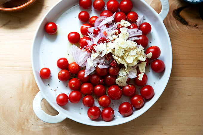 A baking dish filled with tomatoes, shallots, and sliced garlic.