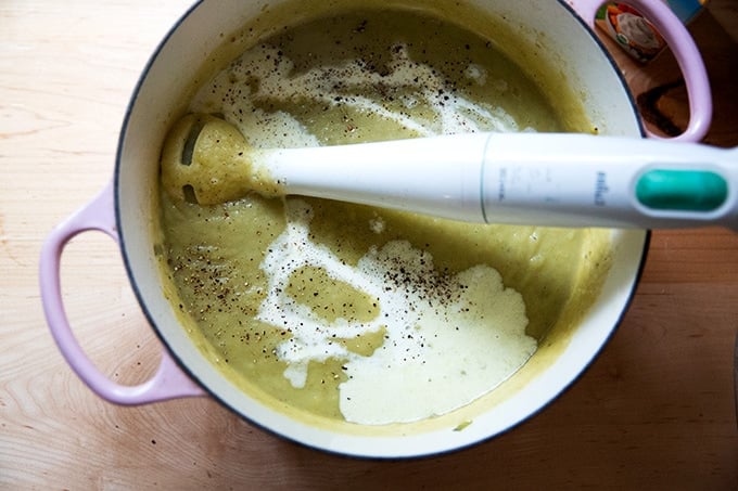 A large pot of potato leek soup being puréed with an immersion blender.