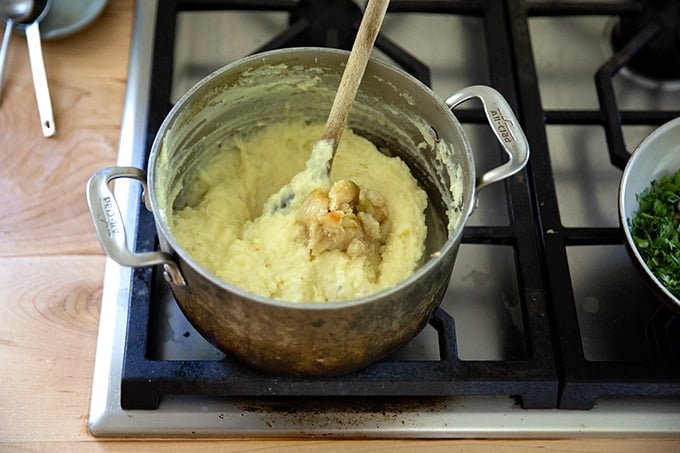 A pot of mashed potatoes on the stovetop with roasted garlic cloves added.