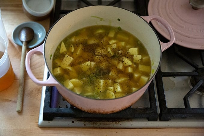 A large pot holding potatoes, leeks, vegetable stock, and pepper, ready to be simmered.