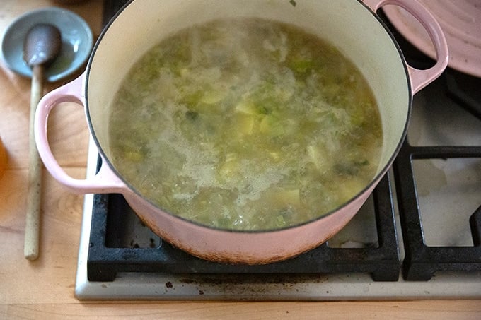 A large soup pot holding potatoes, leeks, and vegetable stock simmering stovetop.