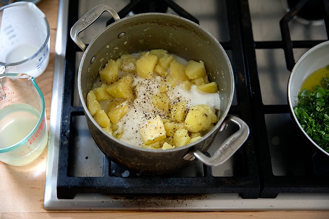 Cooked potatoes in a pot on the stovetop with buttermilk, butter and salt and pepper added.