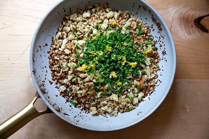 A large skillet holding bread crumbs, chives and lemon zest.