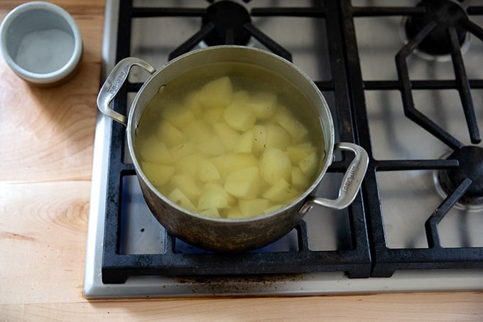 A pot of potatoes on the stovetop covered with cold water.