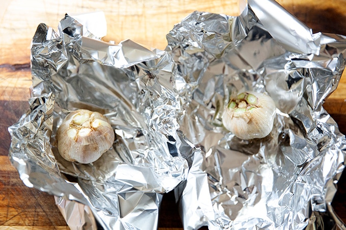 Two heads of garlic each on a sheet of aluminum foil.